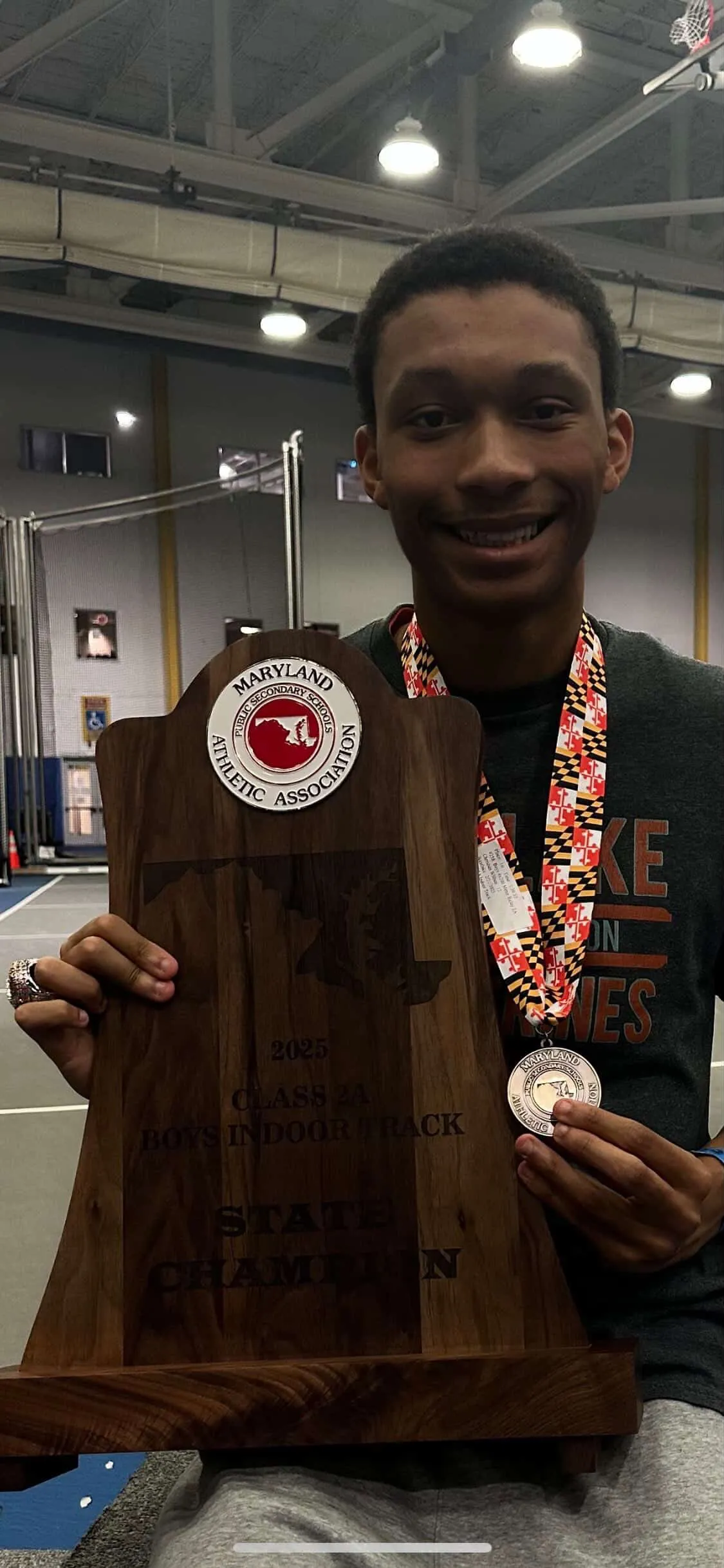 Christian Wilbon holding championship trophy and indoor track medal close up profile